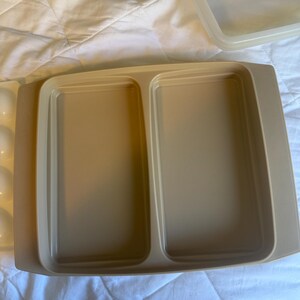 May include: A beige rectangular food storage container with two compartments. The container has a matching lid. The container is made of plastic and is sitting on a white surface.