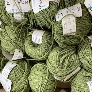 May include: Multiple balls of sage green yarn, each featuring a white paper label with the text Smart, Berroco, 1.75 oz, 87 yds, and care instructions. The yarn is a twisted cord style, and the labels indicate a composition of 68% cotton, 29% rayon, and 3% nylon.