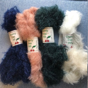 May include: Five skeins of fluffy yarn in various colors: navy blue, peach, dark green, and white. Each skein has a label that reads "Cherry Tree Hill". The yarn appears soft and textured, suitable for knitting or crochet projects.