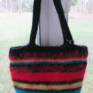 May include: A handmade felted tote bag with black handles and a striped pattern. The bag features horizontal stripes in red, yellow, blue, and black. A small silver charm hangs from one handle.