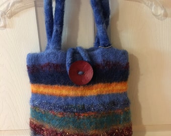 May include: A handmade, felted tote bag with blue, orange, and teal horizontal stripes. The bag has two blue handles and a large, round, red button closure. The bag is approximately 25 cm tall and 20 cm wide.