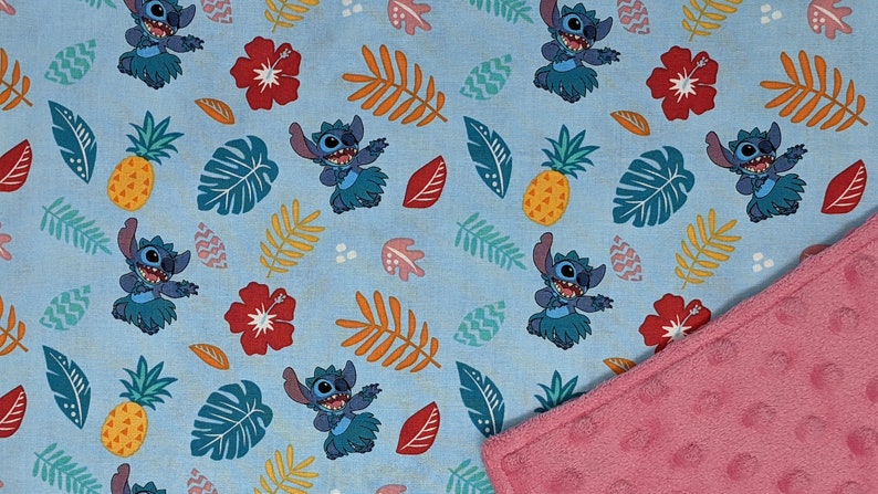 May include: A blue and pink reversible baby blanket featuring a repeating pattern of Stitch from Lilo & Stitch. The pattern includes Stitch dancing in a grass skirt, pineapples, hibiscus flowers, and tropical leaves.
