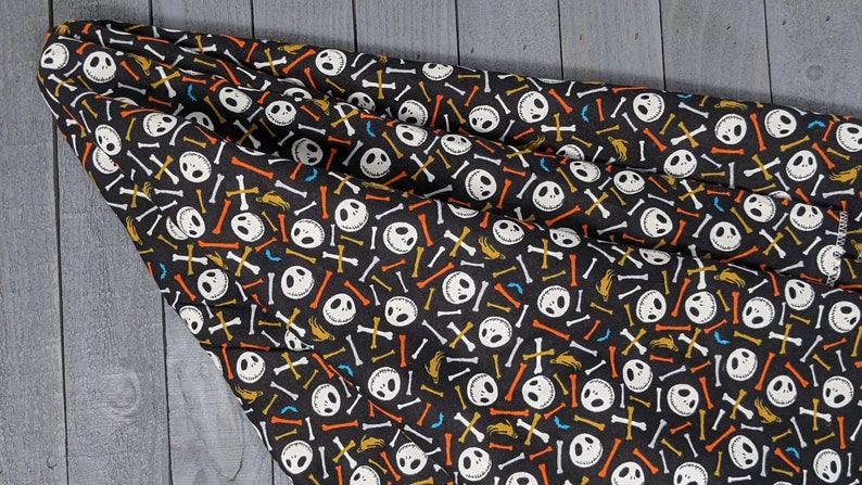 May include: Black fabric with a repeating pattern of white Jack Skellington faces, orange and yellow bones, and white crossbones.