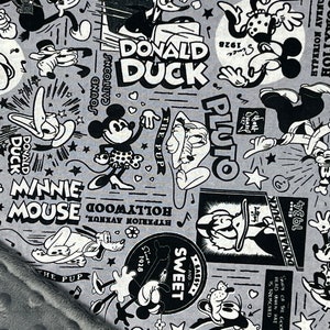 Peut inclure: Tissu gris avec un imprim&eacute; de dessins anim&eacute;s en noir et blanc repr&eacute;sentant Mickey Mouse, Minnie Mouse, Donald Duck et Pluto. Le motif comprend des &eacute;l&eacute;ments textuels tels que "Donald Duck", "Minnie Mouse" et "Pluto", ainsi que des &eacute;toiles et des notes de musique.