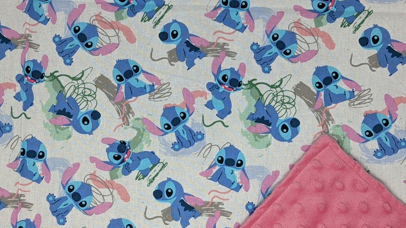 May include: A fabric featuring a repeating pattern of the blue alien character Stitch in various poses, interspersed with green and brown abstract shapes on a light background, with a corner of textured pink dimpled fabric folded over.
