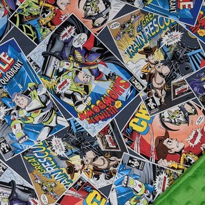 May include: A blue, gray, and white comic book-style blanket featuring characters from the Toy Story franchise. The blanket has a green, textured border. Comic book panels include the words "BATTLE GAMMA QUADRANT", "TRAIN RESCUE", and "SHOWDOWN".