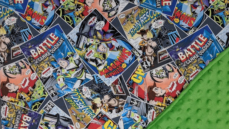 May include: A blue, gray, and white comic book-style blanket featuring characters from the Toy Story franchise. The blanket has a green, textured border. Comic book panels include the words "BATTLE GAMMA QUADRANT", "TRAIN RESCUE", and "SHOWDOWN".