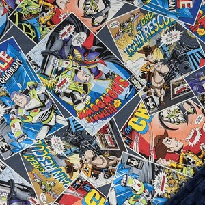 May include: A patterned blanket featuring comic book panels with characters and text. The panels are in various shapes and sizes, with a dark blue background. The text includes "BATTLE", "GAMMA QUADRANT", and "SHOWDOWN". A dark blue, textured fabric is visible in the corner.