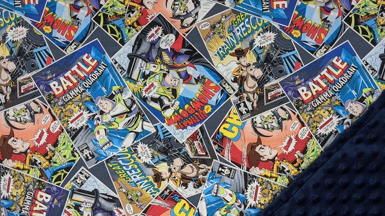 May include: A patterned blanket featuring comic book panels with characters and text. The panels are in various shapes and sizes, with a dark blue background. The text includes "BATTLE", "GAMMA QUADRANT", and "SHOWDOWN". A dark blue, textured fabric is visible in the corner.