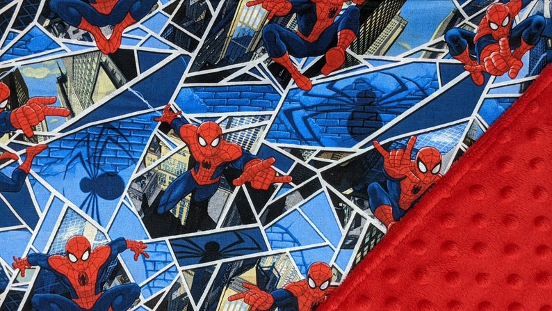 K&ouml;nnte beinhalten: Eine Decke mit einem sich wiederholenden Muster von Spider-Man in Actionposen vor Stadtlandschaften und Spinnennetzen. Die Decke hat einen roten, strukturierten Rand.