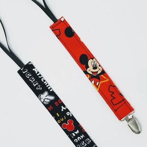 Puede incluir: Dos clips para chupete de beb&eacute;. Uno es rojo con un dise&ntilde;o de Mickey Mouse y un clip plateado. El otro es negro con una mano de Mickey Mouse blanca y texto. Ambos tienen un lazo negro.