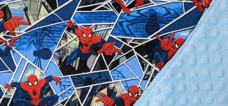 K&ouml;nnte beinhalten: Eine blau-rote Spider-Man-Decke. Das Design zeigt Spider-Man in verschiedenen Action-Posen vor dem Hintergrund von Stadtlandschaften und Spinnennetzmustern. Ein hellblaues, strukturiertes Gewebe ist sichtbar.