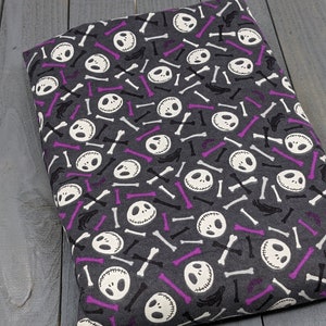 Puede incluir: Tela gris con un patr&oacute;n repetido de caras blancas de Jack Skellington y huesos blancos y morados.