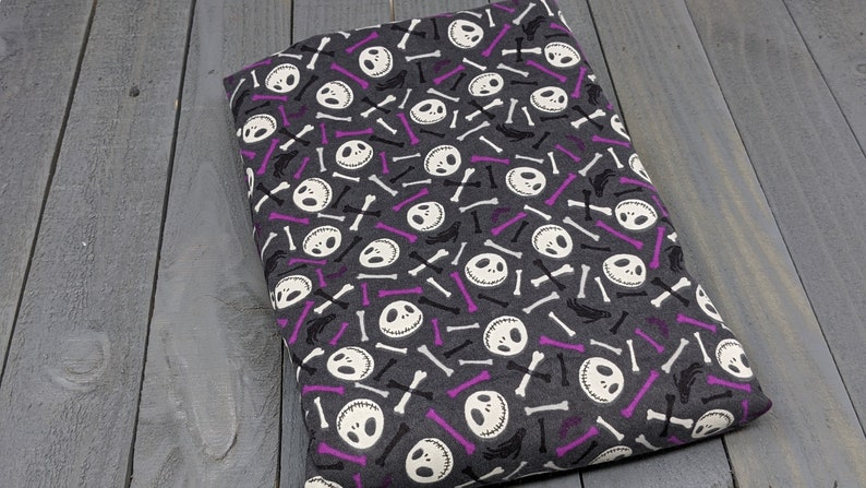 Puede incluir: Tela gris con un patr&oacute;n repetido de caras blancas de Jack Skellington y huesos blancos y morados.