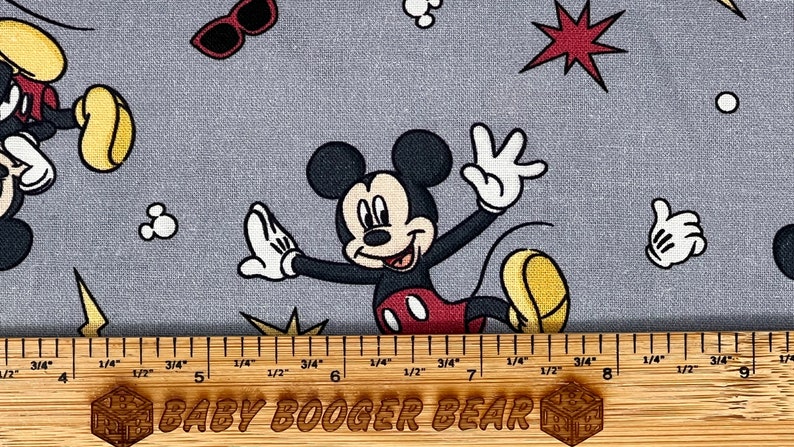 Pu&ograve; includere: Tessuto grigio con un motivo ripetitivo di Topolino in varie pose. Topolino indossa i suoi pantaloncini rossi e le scarpe gialle. Il tessuto presenta anche stelle rosse, punti bianchi e fulmini gialli.