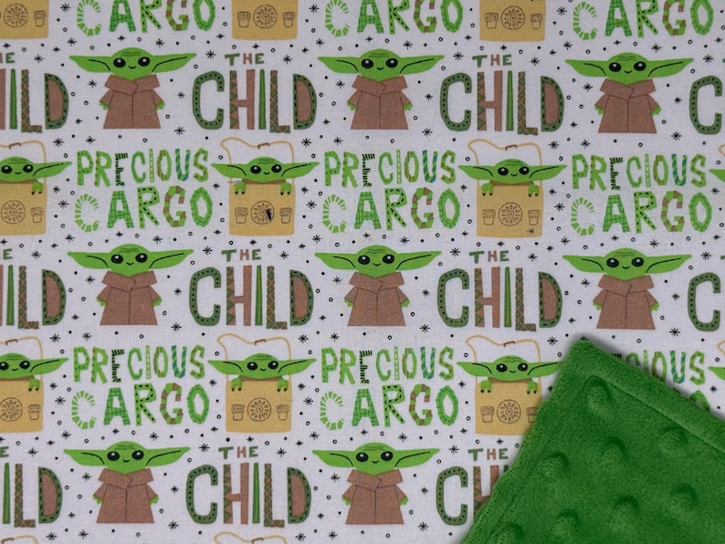 Peut inclure: Tissu blanc avec un motif r&eacute;p&eacute;t&eacute; d'un personnage extraterrestre vert, de robes marron et des mots "THE CHILD" et "PRECIOUS CARGO" en vert. Un coin de couverture vert et textur&eacute; est en bas &agrave; droite.