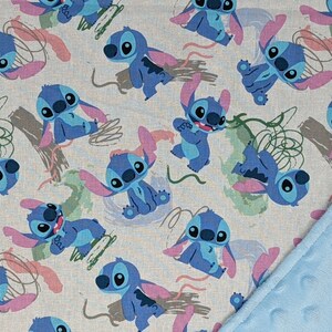 May include: A fabric blanket featuring a repeating pattern of blue Stitch characters on a light gray background, accented with pink ears and green abstract shapes. One corner of the blanket is folded over to reveal a textured, light blue minky fabric.