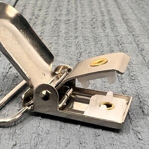 May include: Silver metal clip with a white plastic insert and a gold metal ring. The clip is open and the insert is visible.