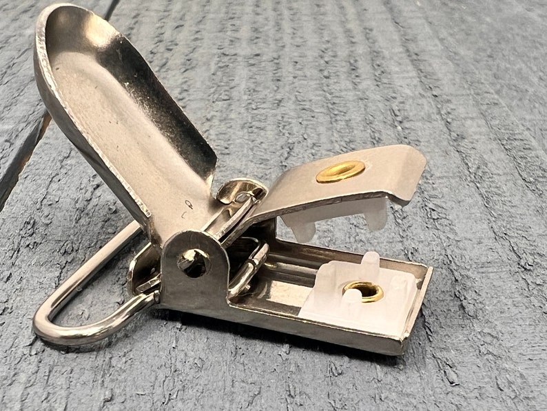 May include: Silver metal clip with a white plastic insert and a gold metal ring. The clip is open and the insert is visible.
