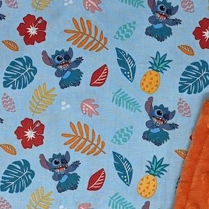 May include: A blue and orange baby blanket with a repeating pattern of Stitch from Lilo & Stitch wearing a grass skirt and dancing. The pattern also includes pineapples, hibiscus flowers, and tropical leaves.