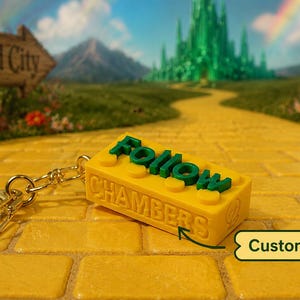 May include: A yellow rectangular building block keychain with a gold metal ring. The block features the green raised text Follow and the embossed text CHAMBERS on the side. A small arrow points to the text with a label that reads Customizable!