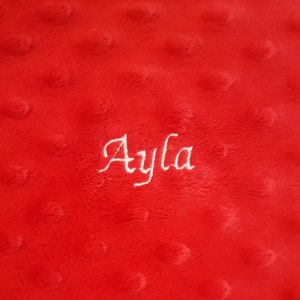 Puede incluir: Manta de felpa roja con el nombre "Ayla" bordado en hilo blanco.