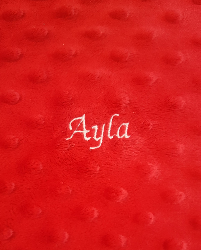 Puede incluir: Manta de felpa roja con el nombre "Ayla" bordado en hilo blanco.