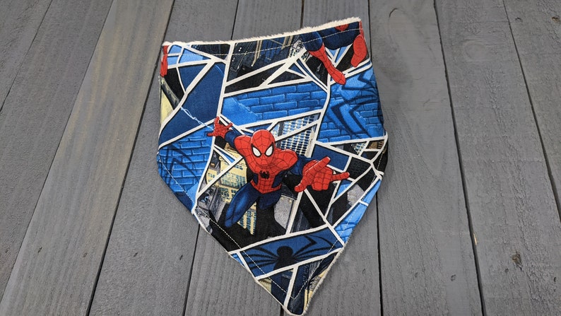 K&ouml;nnte beinhalten: Ein blau-wei&szlig;es Bandana mit einem Spider-Man-Design. Das Bandana hat ein geometrisches Muster mit Bildern von Spider-Man in Aktion. Die Kanten sind mit einem wei&szlig;en Besatz versehen. Dieses Accessoire ist f&uuml;r Haustiere geeignet.