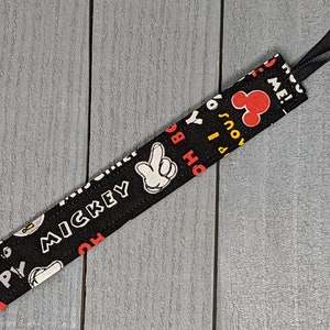 Peut inclure: Un attache-t&eacute;tine noir et blanc sur le th&egrave;me de Mickey Mouse avec un clip en m&eacute;tal argent&eacute;. Le tissu pr&eacute;sente la main, le visage et le mot "Mickey" de Mickey Mouse. Le clip a un ruban noir attach&eacute;.