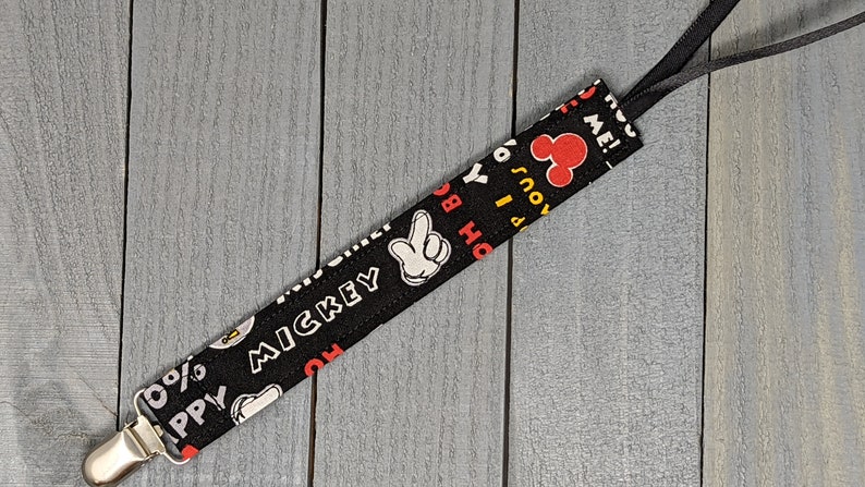 Peut inclure: Un attache-t&eacute;tine noir et blanc sur le th&egrave;me de Mickey Mouse avec un clip en m&eacute;tal argent&eacute;. Le tissu pr&eacute;sente la main, le visage et le mot "Mickey" de Mickey Mouse. Le clip a un ruban noir attach&eacute;.