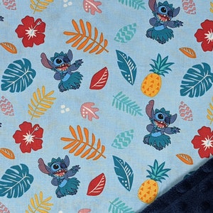 May include: Blue fabric with a repeating pattern of Stitch from Lilo & Stitch wearing a grass skirt, pineapples, hibiscus flowers, and tropical leaves.
