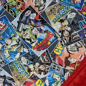 May include: A patterned fabric featuring comic book panels with characters and text like "BATTLE GAMMA QUADRANT" and "SHOWDOWN". A red, textured fabric is diagonally placed over the patterned fabric.