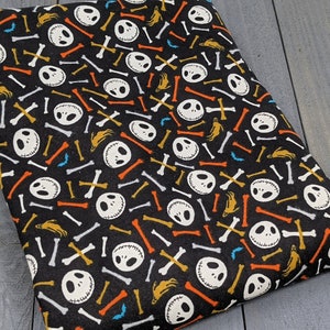 May include: Black fabric with a repeating pattern of white Jack Skellington faces and colorful bone shapes.