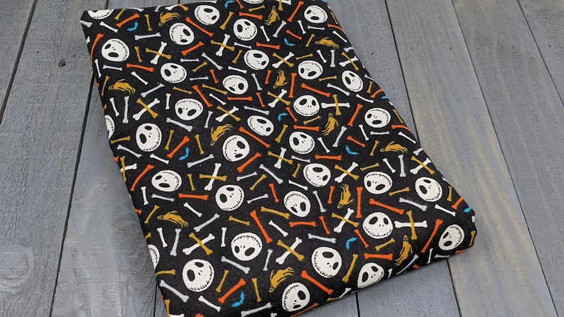 May include: Black fabric with a repeating pattern of white Jack Skellington faces and colorful bone shapes.