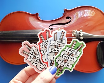 May include: Four colorful stickers with the text "Proud Orch Dork" on a violin. The stickers are in red, blue, green, and pink.