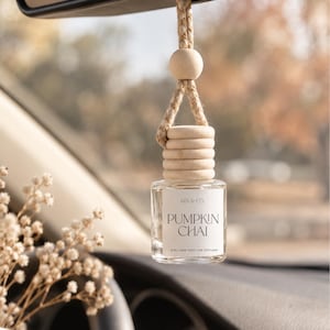 May include: A clear glass car diffuser bottle with a light wood cap and a matching wooden bead on a braided rope. The white label features the text KEN & CO, PUMPKIN CHAI, and 8 ML NON TOXIC CAR DIFFUSER in black, sans-serif lettering.