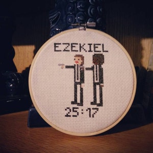 May include: A white embroidery hoop with the text "Ezekiel 25:17" and two figures in black suits with white shirts and black ties.