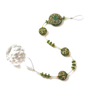 May include: A crystal ball hanging from a silver chain with green and gold beads. The beads have a swirling pattern and are interspersed with smaller green beads.