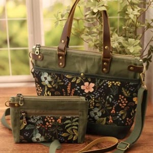 Puede incluir: Dos bolsos de lona verde con estampados florales y asas de cuero marr&oacute;n. El bolso m&aacute;s grande tiene una correa para el hombro. El bolso m&aacute;s peque&ntilde;o tiene una cremallera.
