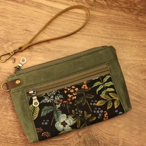 Puede incluir: Una bolsa de lona verde con cremallera y forro de estampado floral. La bolsa tiene una correa de cuero marr&oacute;n con un cierre de metal.