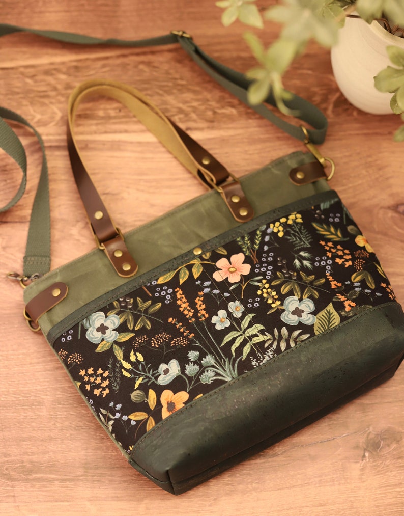 Puede incluir: Un bolso tote de lona verde con estampado floral y correas de cuero marr&oacute;n. El bolso tiene cierre de cremallera y una correa larga para llevarlo al hombro.
