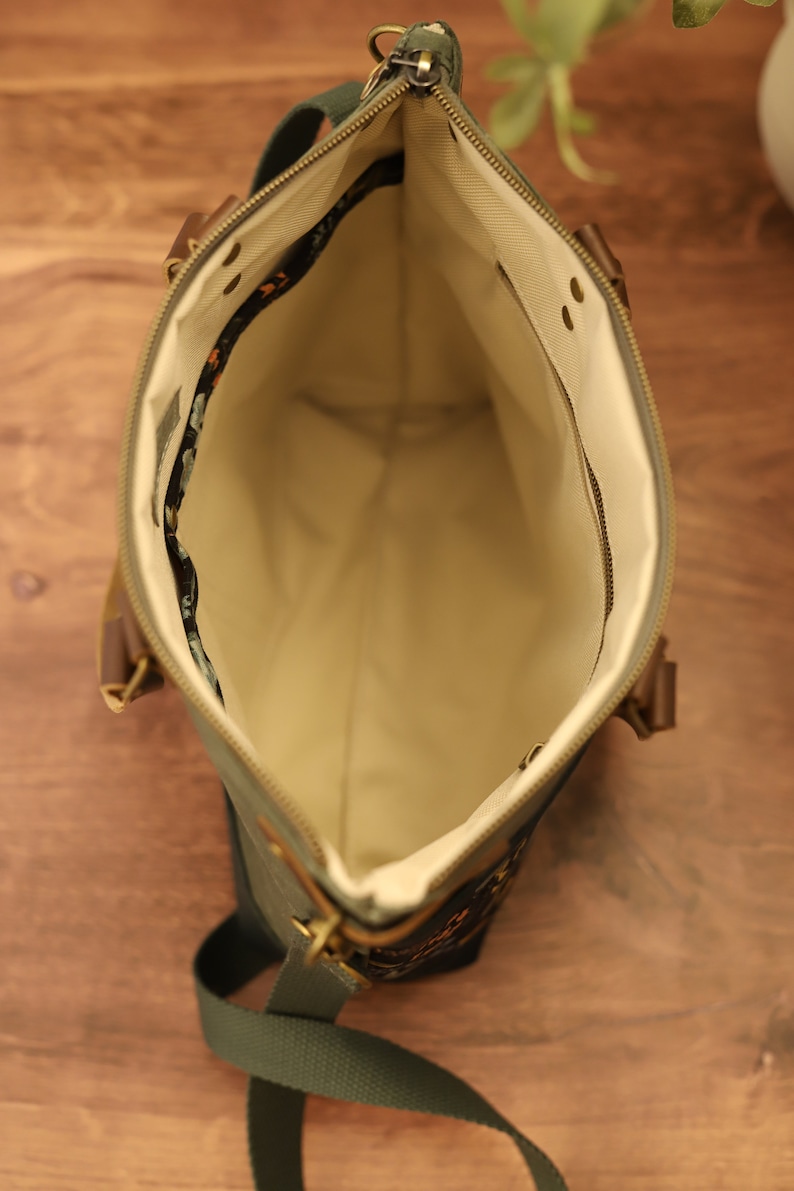 Puede incluir: Un bolso tote de lona verde con cierre de cremallera y una correa larga ajustable. El bolso tiene un forro beige y un peque&ntilde;o bolsillo interior.