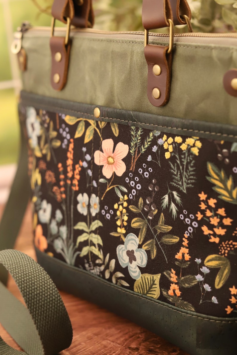 Puede incluir: Un bolso tote de lona verde con un forro de estampado floral. El bolso tiene asas de cuero marr&oacute;n y cierre de cremallera. El bolso tambi&eacute;n tiene una correa larga verde.