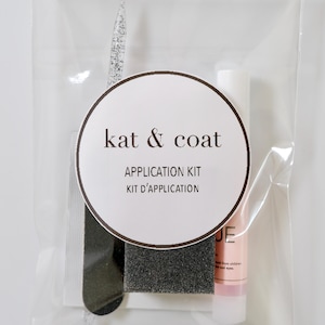 May include: A clear plastic bag containing a nail application kit. The kit includes a nail file, buffer, and a tube of nail product. The kit is labeled "kat & coat APPLICATION KIT KIT D'APPLICATION".