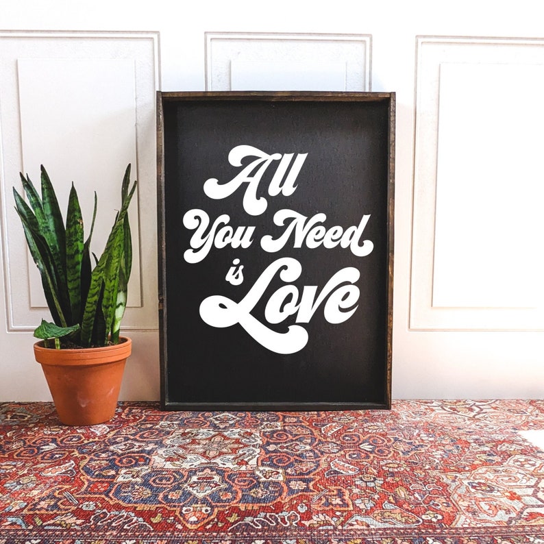 a framed wood sign with a black background with 'all you need is love' written on it in white font