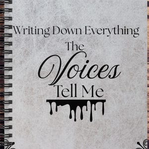Op de afbeelding: Een spiraalgebonden notitieboek met een getextureerde, lichtgrijze kaft. De kaft bevat de tekst "Writing Down Everything The Voices Tell Me" in zwart script. Een donkerrode pen met gouden accenten ligt naast het notitieboek op een houten oppervlak.
