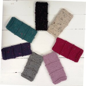May include: Eight knitted wrist warmers in different colors and patterns. The warmers are arranged in a circle on a white wooden surface.