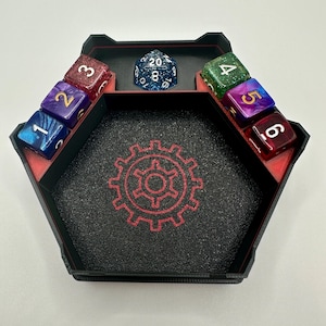 May include: A black and red hexagonal dice tray with a red gear design in the center. The tray has six compartments for dice, each with a number from 1 to 6. A blue 20-sided die is in the center of the tray.