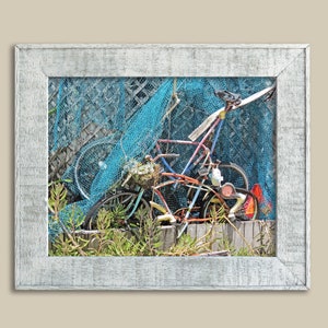 Pode incluir: Uma fotografia emoldurada de uma bicicleta e outros objetos, parcialmente obscurecidos por uma rede de pesca azul, contra um fundo de madeira.