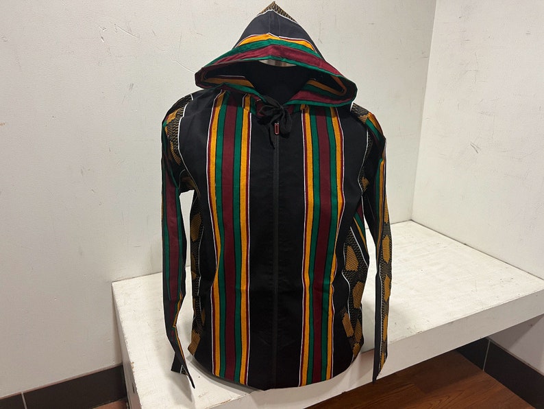 Pu&ograve; includere: Una giacca nera con cappuccio e chiusura a zip. La giacca ha un motivo a righe in rosso, verde e giallo.